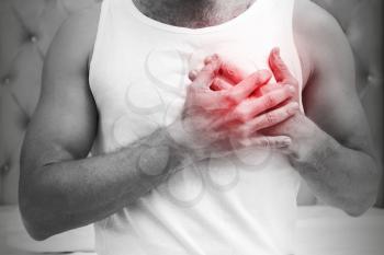 Heart pain gesture. Young sporty Caucasian man in white shirt holds hands near his heart. Black and white stylized photo with red local ache spot