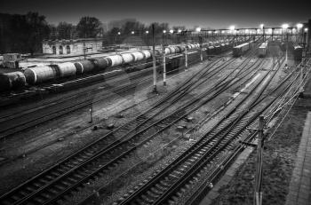 Sorting railway station with cargo trains on rails at night, black and white photo