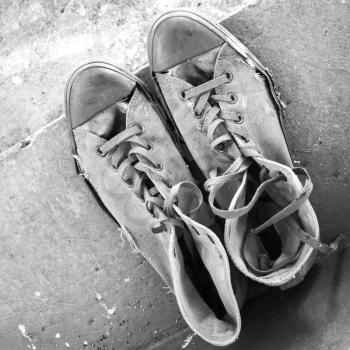Pair of old sneakers standing on concrete stairs, top view. Black and white retro stylized photo
