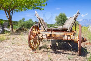Empty old rural wooden wagon stands on summer field under clouded sky. Zakynthos island, Greece
