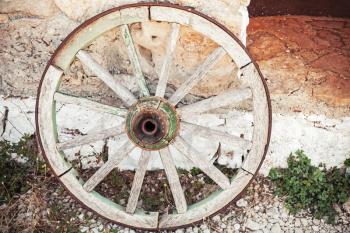 Old wooden wheel stands near stone rural wall