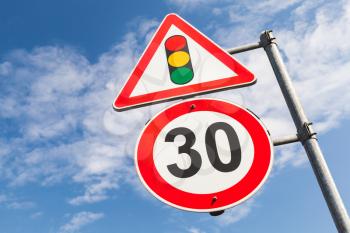 Traffic lights and speed limit 30 km per hour mounted on metal post. Road signs over blue sky background