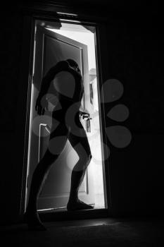 Young man stands near door in black room and looks inside opening to the light, black and white photo