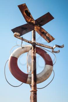Old rusted cross shaped navigation sign with lifebuoy 