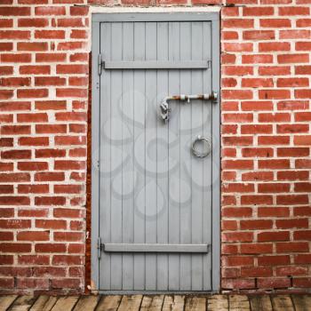 Locked gray wooden door in old red brick wall, square background photo texture