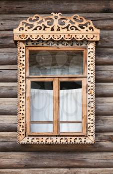 Traditional rural Russian ancient architecture details. Window with carved wooden frame in wall made of rough logs