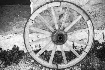 Old wooden wheel stands near stone rural wall, black and white retro style photo