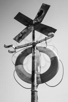 Old rusted cross shaped navigation sign with lifebuoy, black and white retro style photo