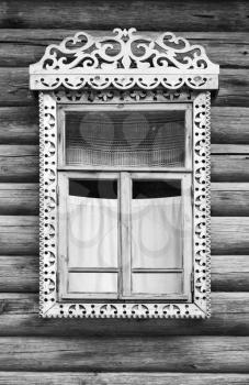 Traditional rural Russian ancient architecture details. Window with carved wooden frame in wall made of rough logs, black and white retro style photo