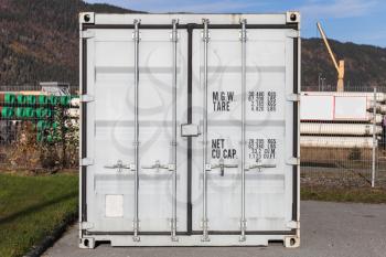 Closed white standard cargo container stands in port area, door face, closeup photo with selective focus