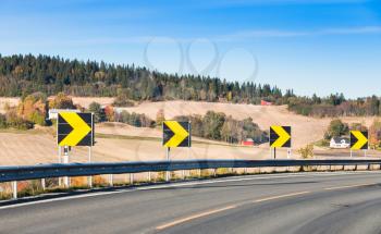 Dangerous turn. Yellow arrows in black square roadsigns along turning highway, rural Norwegian road