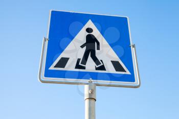 Pedestrian crossing. Square blue and white road sign with schematic walking man over blue sky background