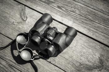 Black touristic binoculars lays on rough outdoor wooden table