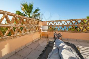 Feet of man relaxing on sun lounger, seaside balcony, popular touristic resort Zakynthos island, Greece
