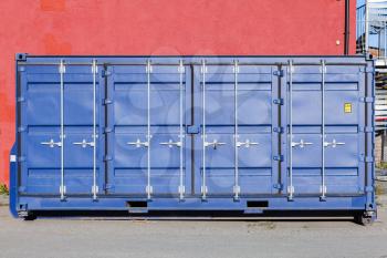 Closed blue standard cargo container stands in port area, side doors face