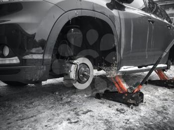 Replacing wheels on new black SUV car, two jacks hold the body in the raised position