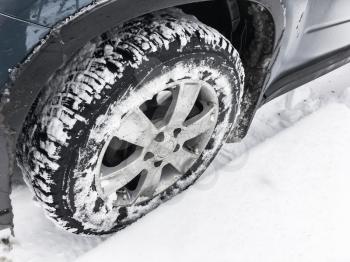 Modern car fragment, wheel with studded tire standing on winter road with deep snow, close-up photo with selective focus