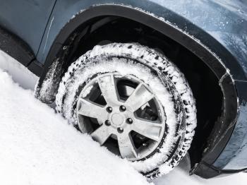Modern blue car fragment, wheel with studded tire standing on winter road with deep snow