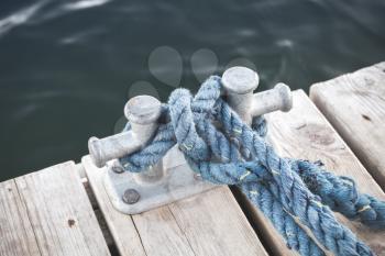 Mooring bollard with tied blue rope mounted on white wooden pier, yacht marina safety equipment