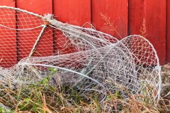 Old fishing traps with net lay near red wooden wall in small Norwegian fishing village