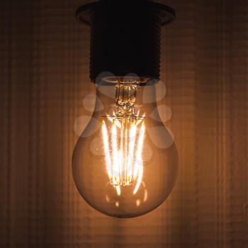 Retro tungsten lamp glowing over empty wall, square photo with selective focus and shallow DOF