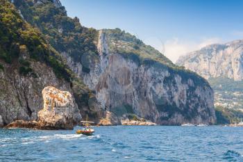 Small touristic motorboat goes near rocks of Capri, Italian island
