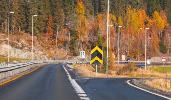 Divarication of rural Norwegian road with warning striped roadsign in autumn season