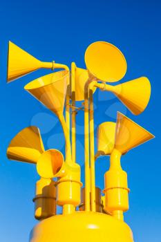 Group of bright yellow loudspeakers over blue sky background, vertical photo