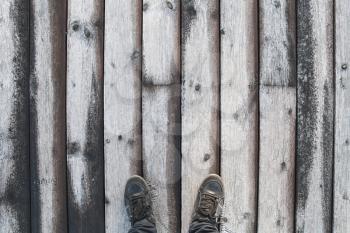 Male feet in black leather shoes stand on old wooden pier floor with frost