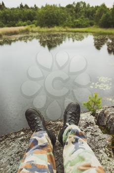 Male feet in camouflage pants and black rough shoes. Vertical travel lifestyle background. Vintage tonal correction photo filter, old style effect