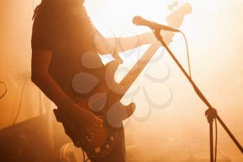 Silhouette of bass guitar player on the stage with microphone and bright warm illumination, live music theme
