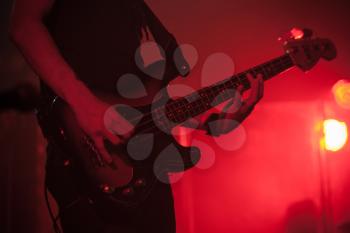 Silhouette of bass guitar player on the stage with red illumination, hard rock music theme