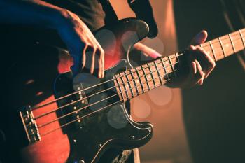 Closeup vintage toned photo of bass guitar player hands, soft selective focus, live music theme, old style filter effect