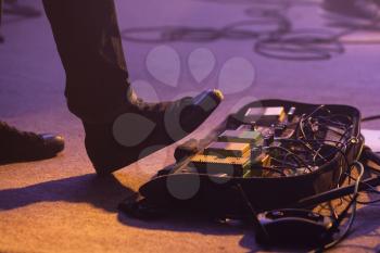 Electric bass guitar player on a stage with set of distortion effect pedals under his foot. Selective focus
