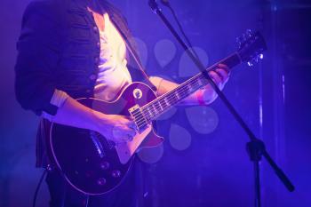 Electric guitar player on a stage with blue scenic illumination, soft selective focus