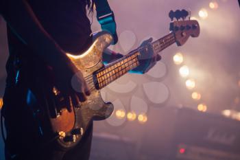 Live rock music background, electric bass guitar player, closeup photo with soft selective focus