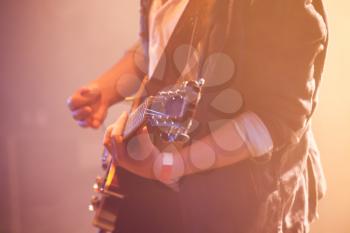 Electric guitar player on a stage with warm scenic illumination, soft selective focus
