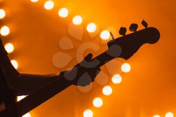 Live music background, electric bass guitar player over bright blurred stage lights, close-up silhouette photo with soft selective focus