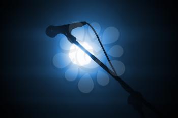 Professional stage microphone in bright spot light over dark blue background