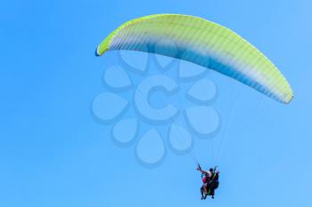 Paragliding in blue sky, tandem of instructor and beginner under green parachute 
