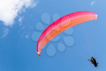 Paragliders in blue sky with clouds, tandem of instructor and beginner under red parachute