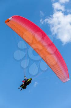 Paragliding in blue sky with clouds, tandem of instructor and beginner under red parachute, vertical photo