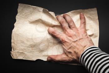Strong sailor hand catching empty old crumpled paper sheet over black background, pirate map concept