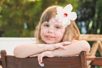 Cute smiling Caucasian little girl with white flower in hair, close-up outdoor portrait