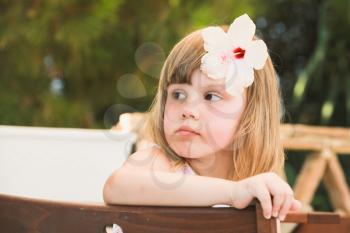 Thinking Cute Caucasian little girl with white flower in hair, close-up outdoor portrait