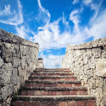 Ancient stone stairway goes up under blue cloudy sky background
