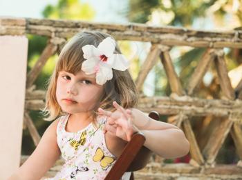 Serious Caucasian little girl with white flower in hair, outdoor portrait