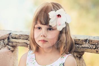 Serious Caucasian little girl with white flower in hair, close-up outdoor portrait, photo with old style tonal correction filter effect