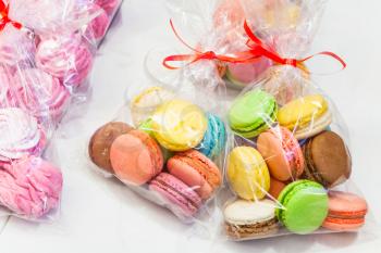 Packs of colorful traditional French macarons and pink meringues lay on market counter