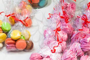 Packs of colorful traditional French macarons and pink meringues lay on white market counter